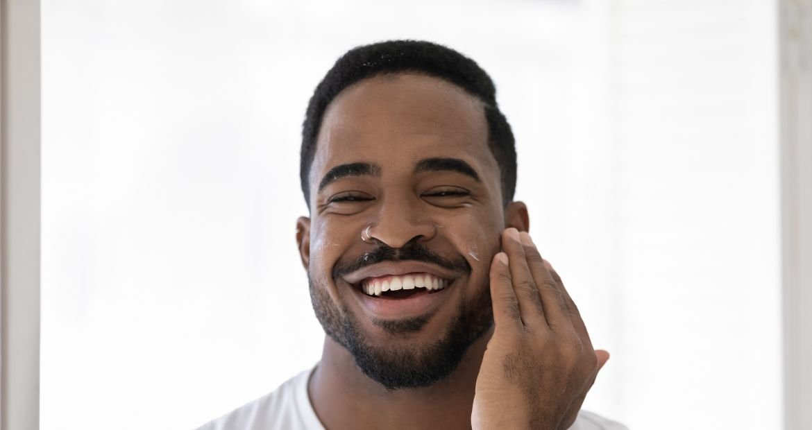 Homem negro sorridente utiliza creme hidratante masculino em sua rotina de skincare masculina